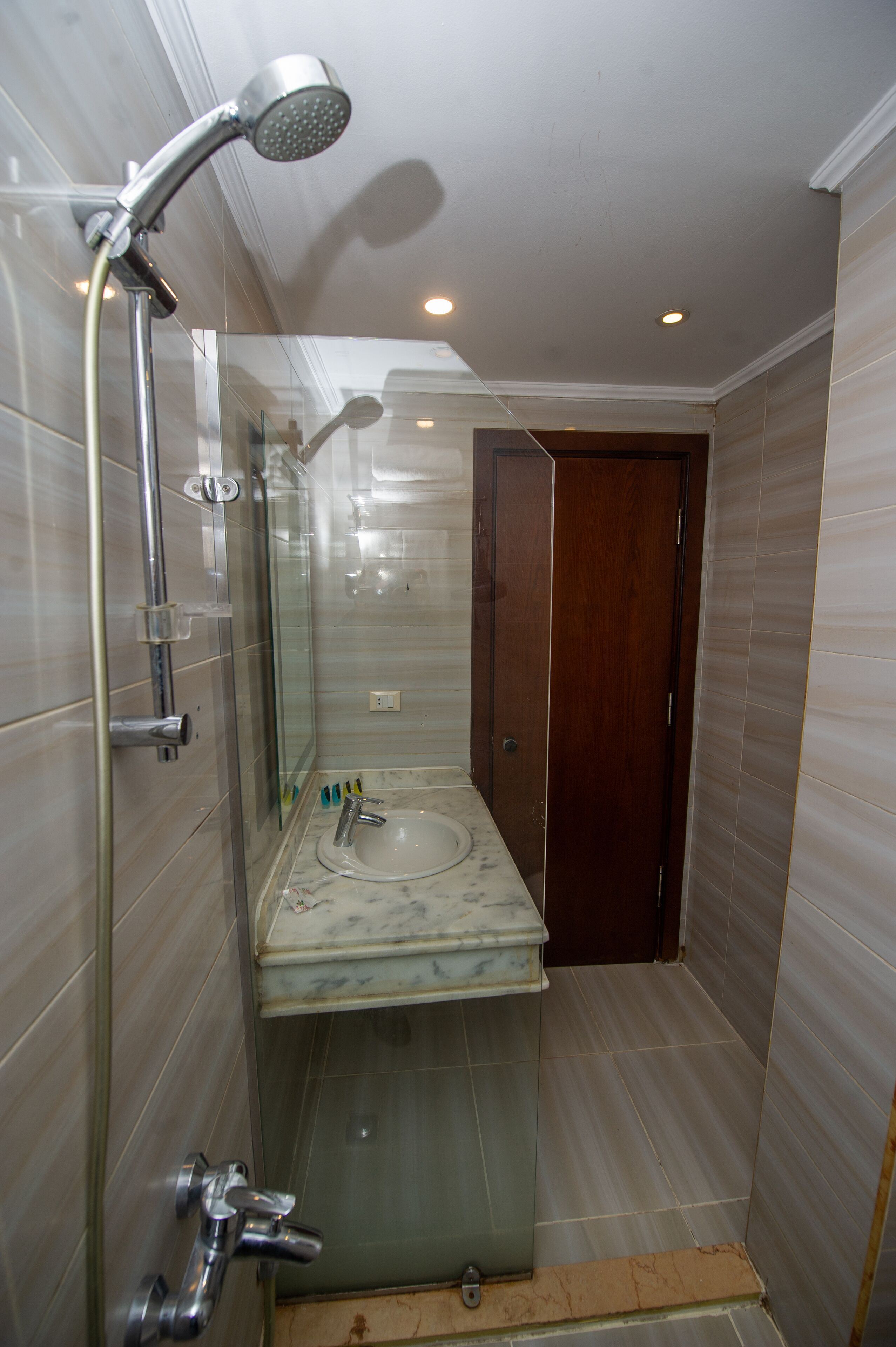 A bathroom with a glass shower enclosure, a sink with a marble countertop, and a wooden door.