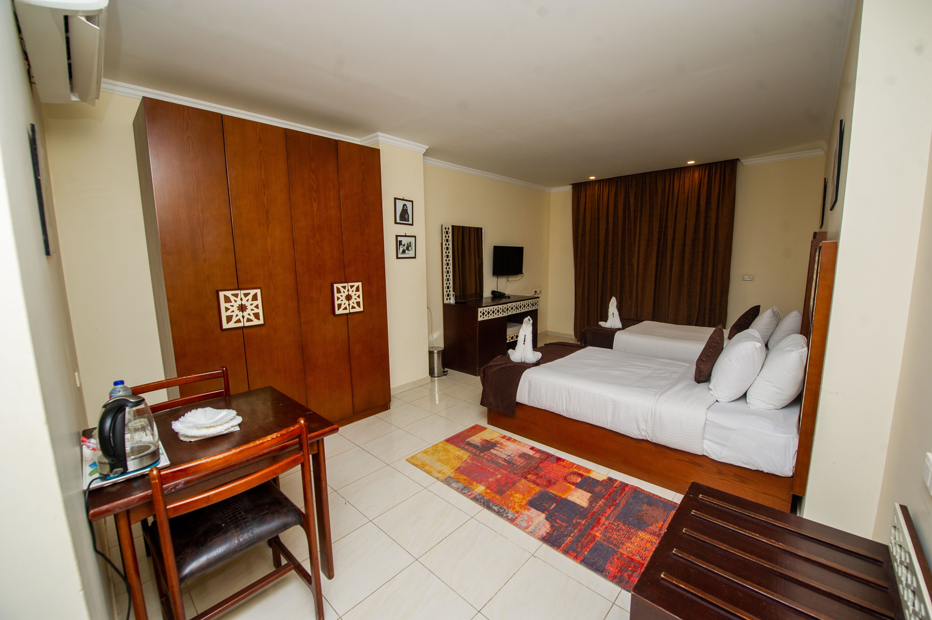 A hotel room with a bed, a desk, a chair, a TV, and a wardrobe.