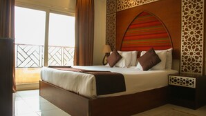 A hotel room with a large bed, a nightstand, a decorative headboard, and a view through a window with curtains. - Pyramids Valley (Giza)