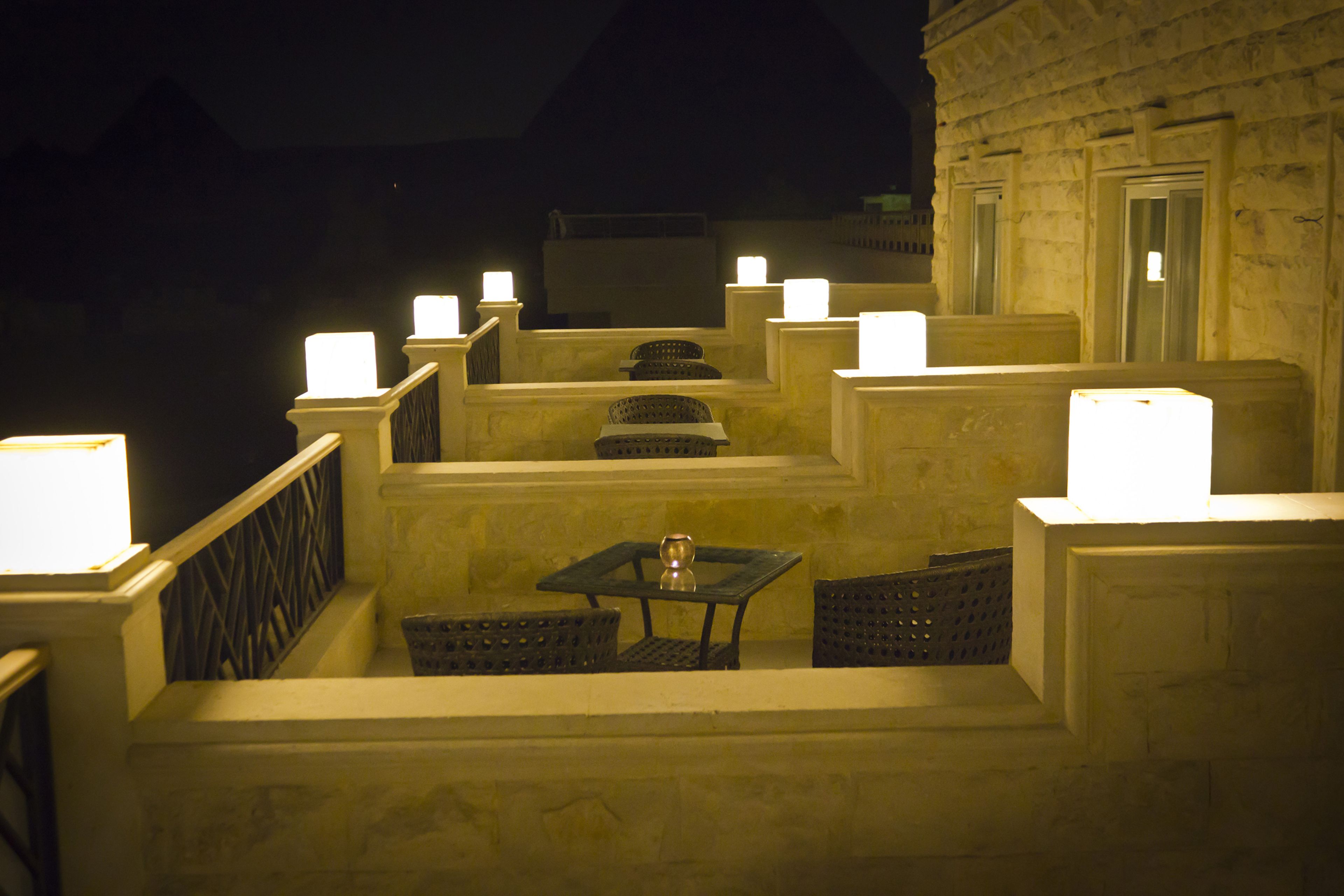 A terrace with a table and chairs, a railing, and multiple illuminated candles.
