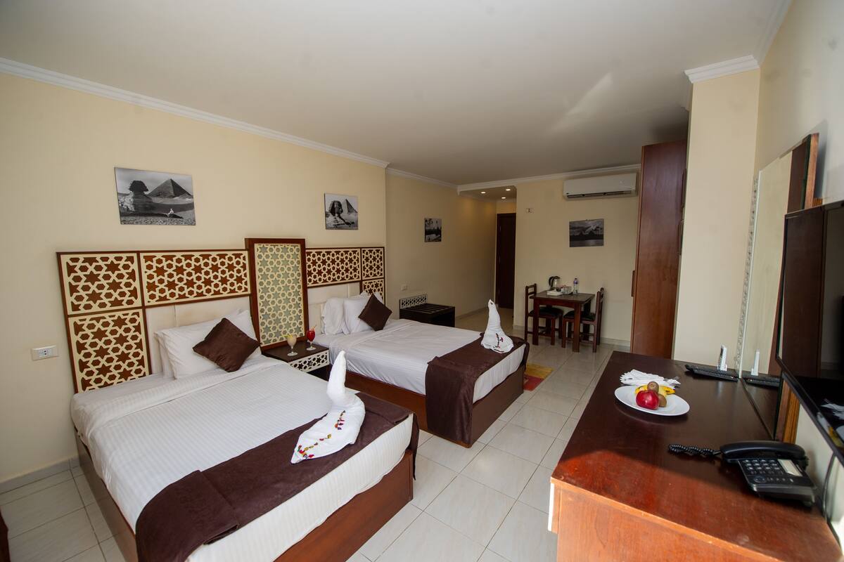 A hotel room with two beds, a desk with a telephone, and a dining area with a table and chairs.