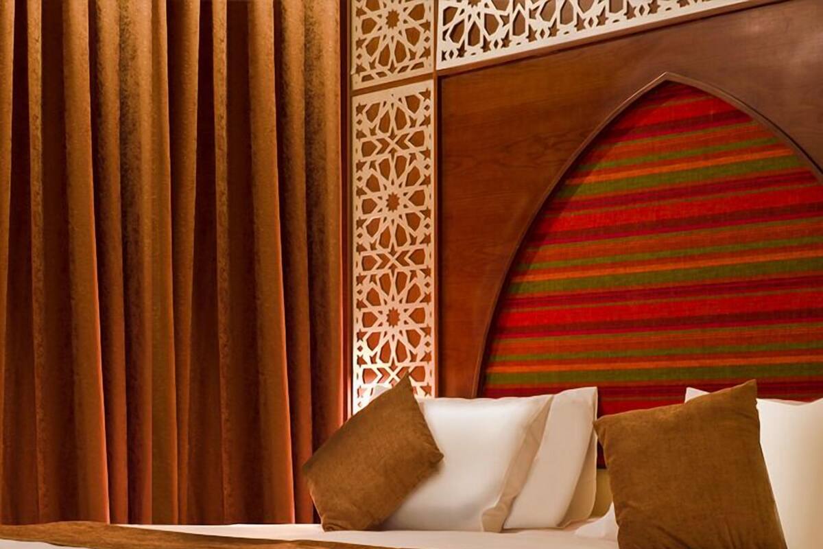 A hotel room with a large bed, brown curtains, and a decorative wall panel.