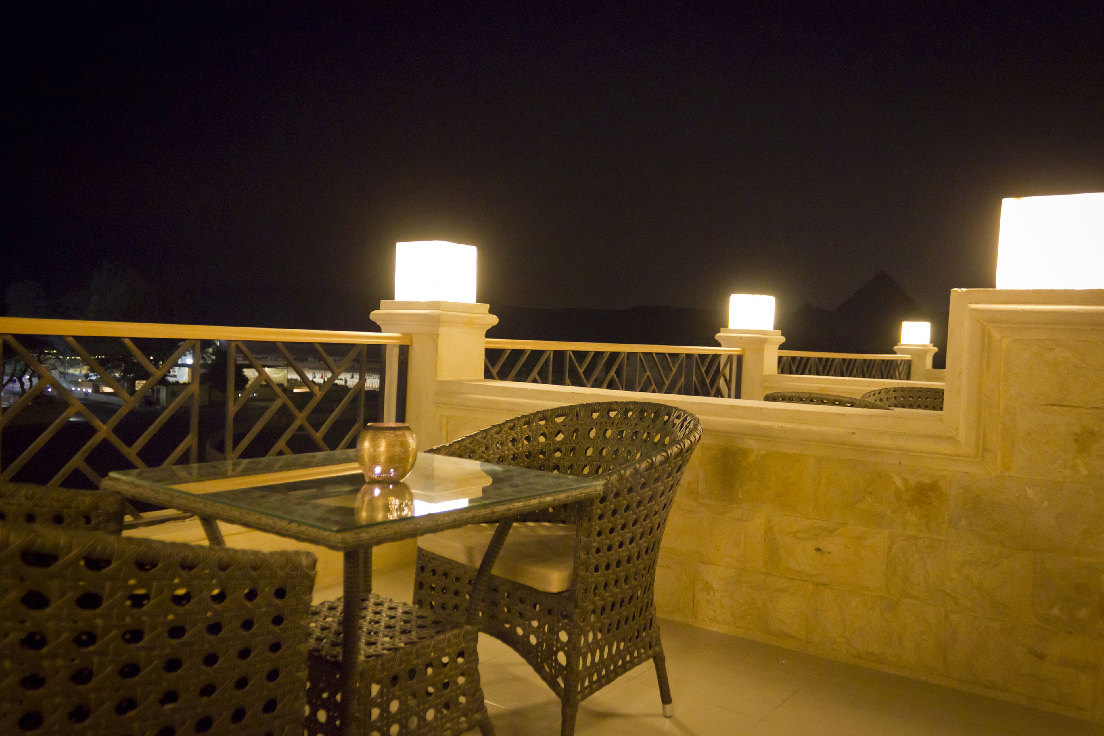 An outdoor terrace with a table and chairs, a glass-top table, and two illuminated lamps.
