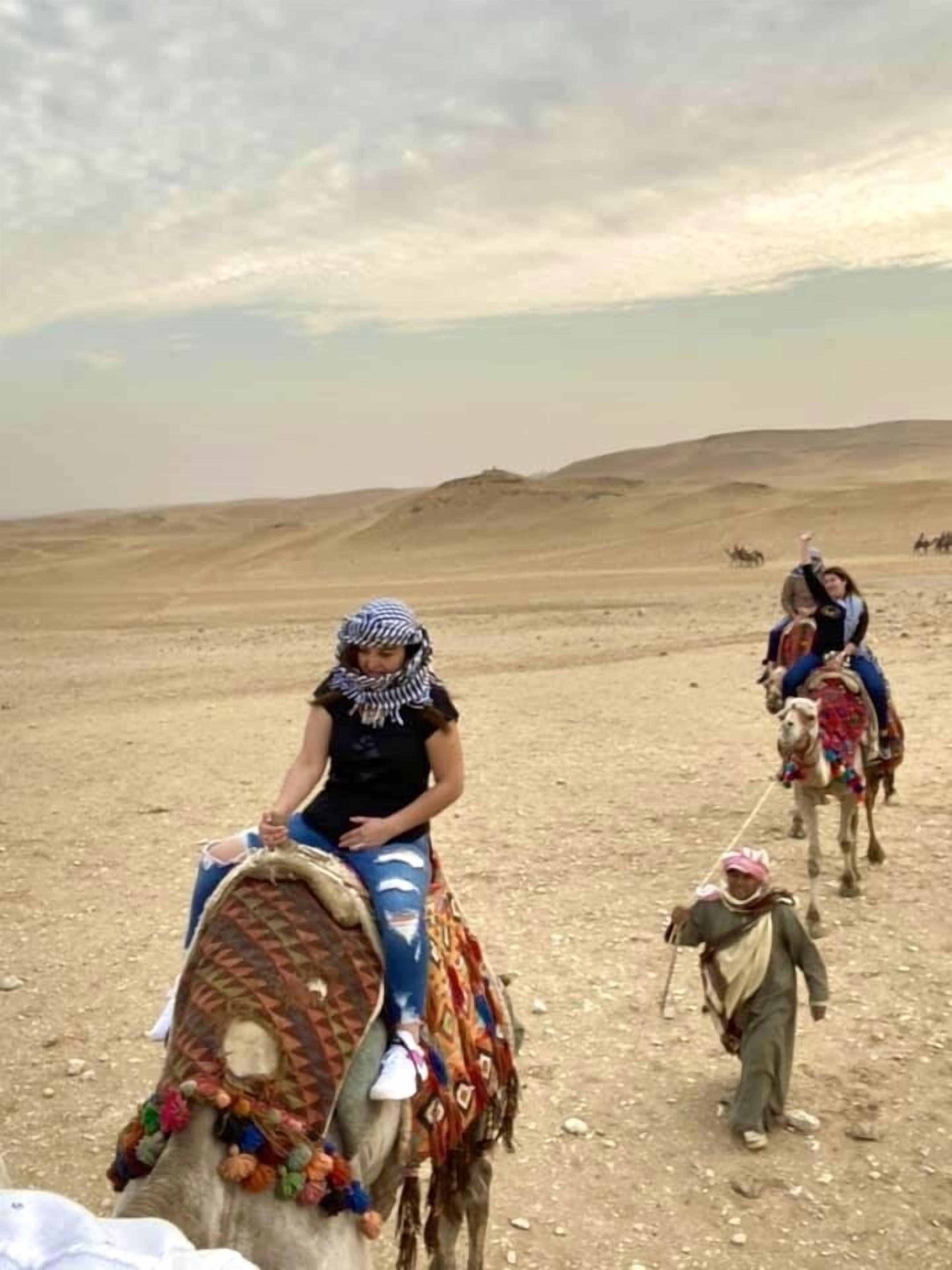 A desert landscape with people riding camels.