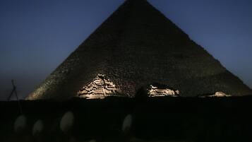 A pyramid-shaped structure illuminated at night, with a stone wall and a small table with a bottle in the foreground.