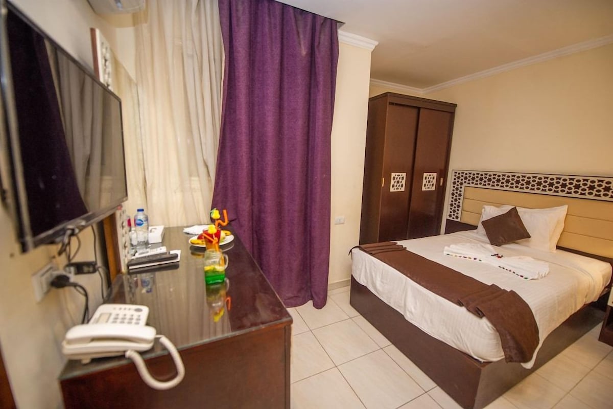 A hotel room with a bed, a desk with a telephone, a TV, and a bathroom door.