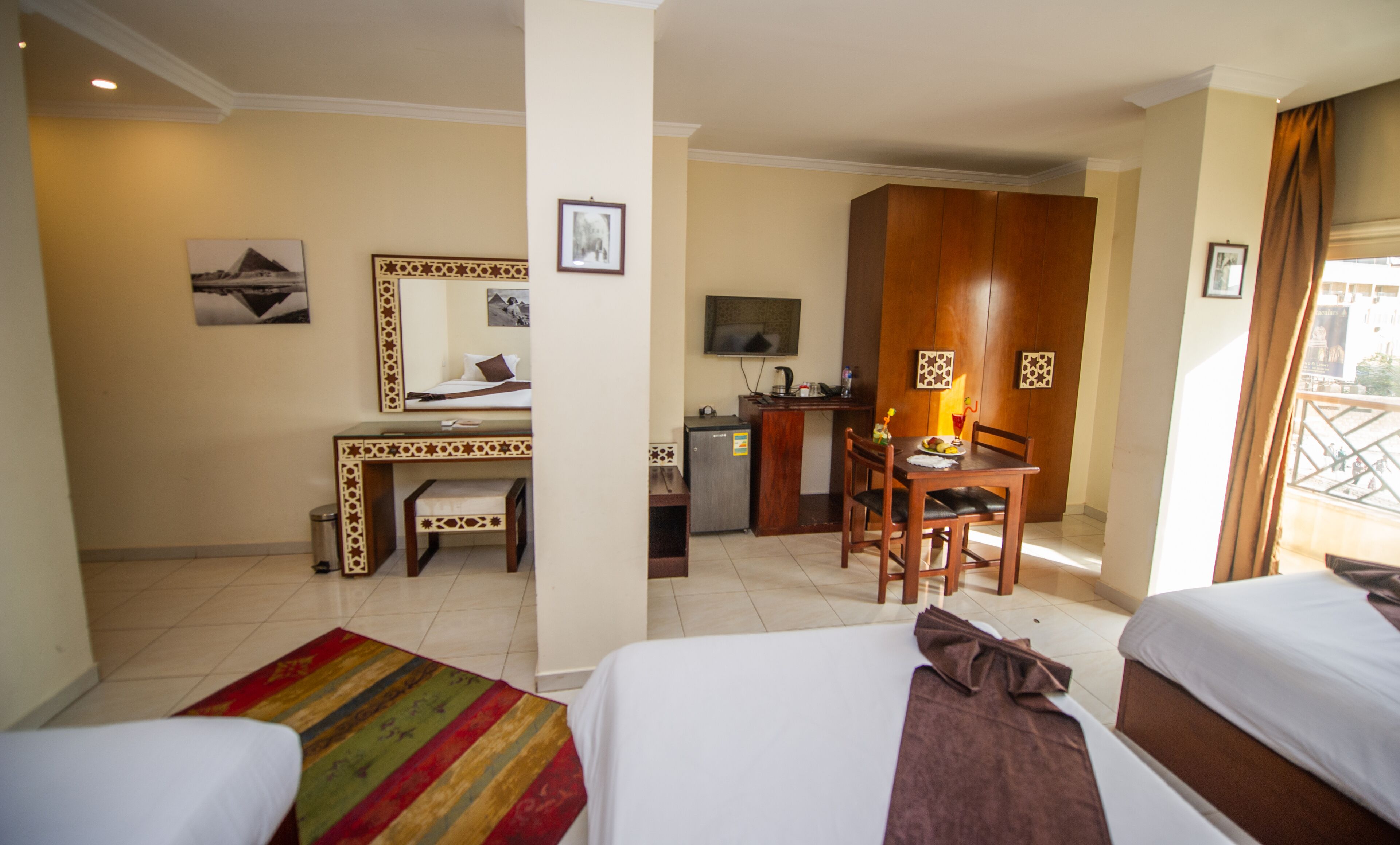 Quarto de hotel com duas camas, uma escrivaninha, uma cadeira, um pequeno frigorífico e uma televisão.