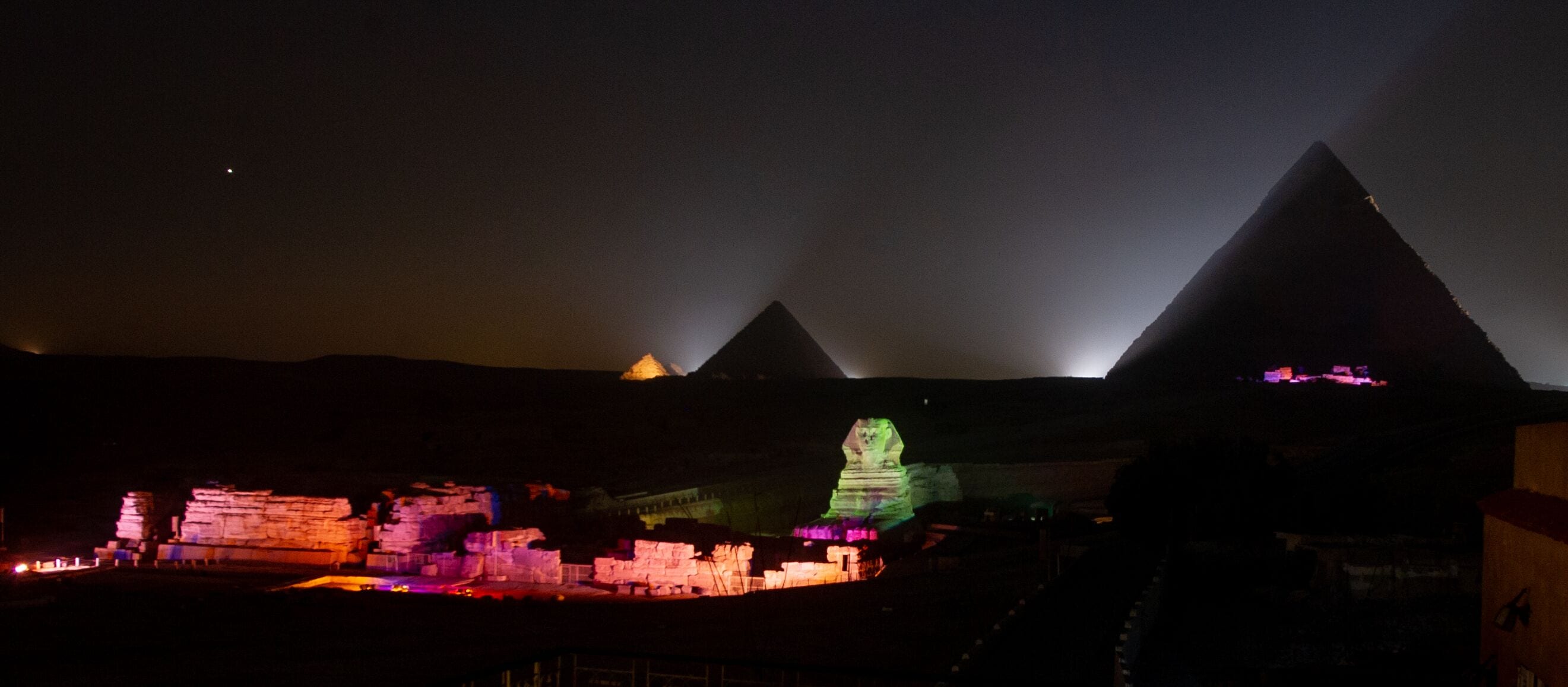 Vista nocturna de las pirámides con estructuras iluminadas en primer plano.