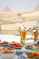 A dining table with a variety of food items and a drink with a straw, set against a backdrop of pyramids.