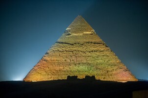 A large pyramid structure with a broad base and a pointed top, illuminated against a dark sky.
