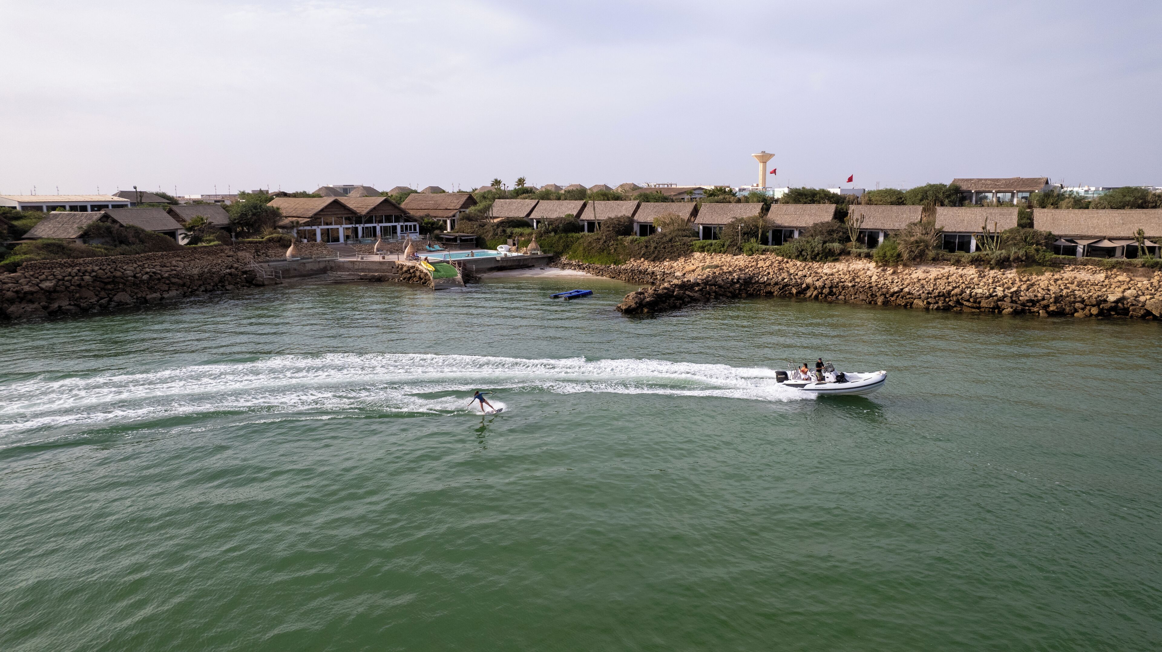 Un río con barcos, un muelle y edificios con techos de paja.