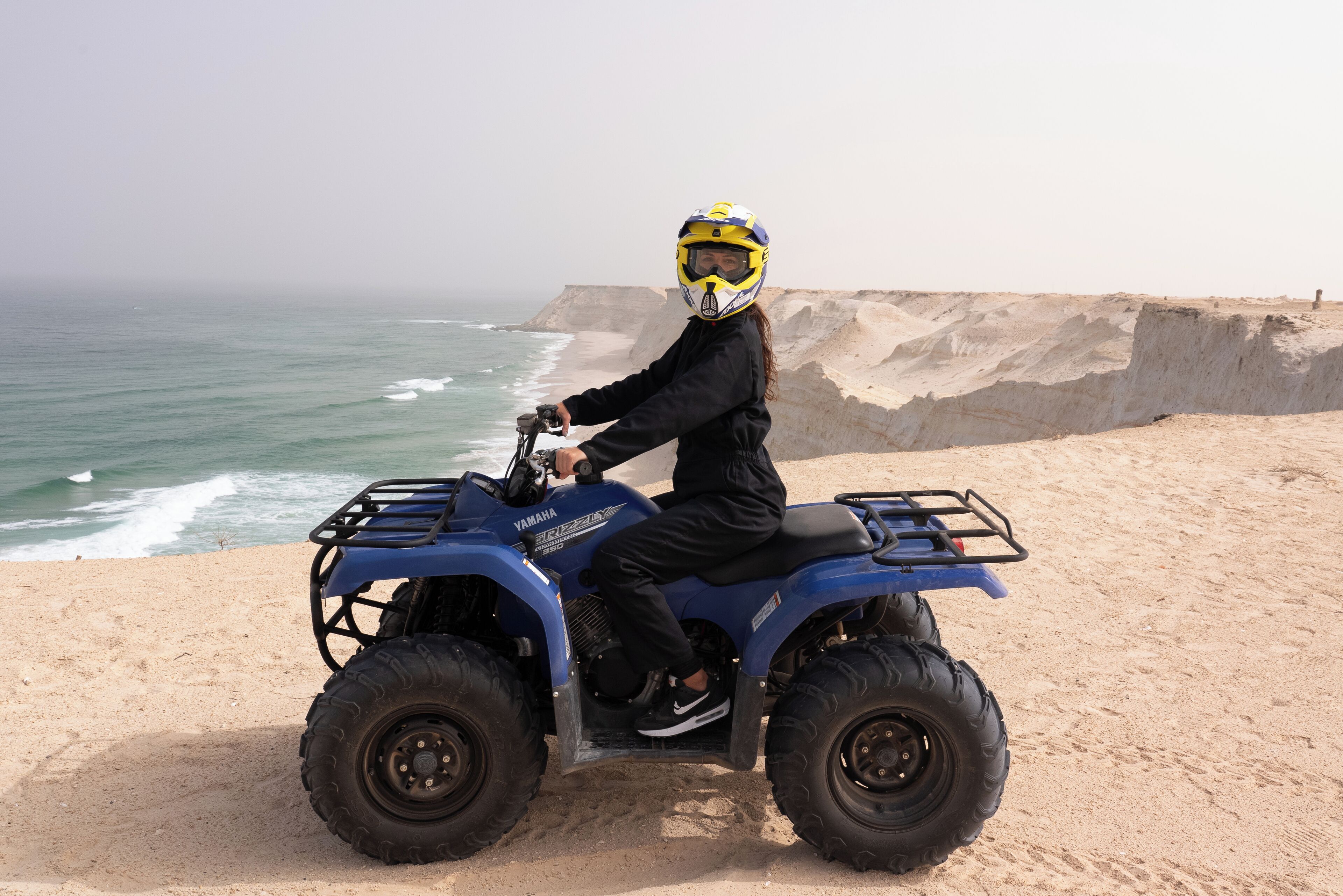 A person riding a blue Yamaha ATV on a sandy beach with the ocean in the background.