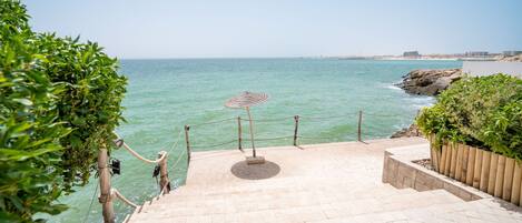 A staircase leading to a beach with a rope barrier and a traditional woven umbrella.