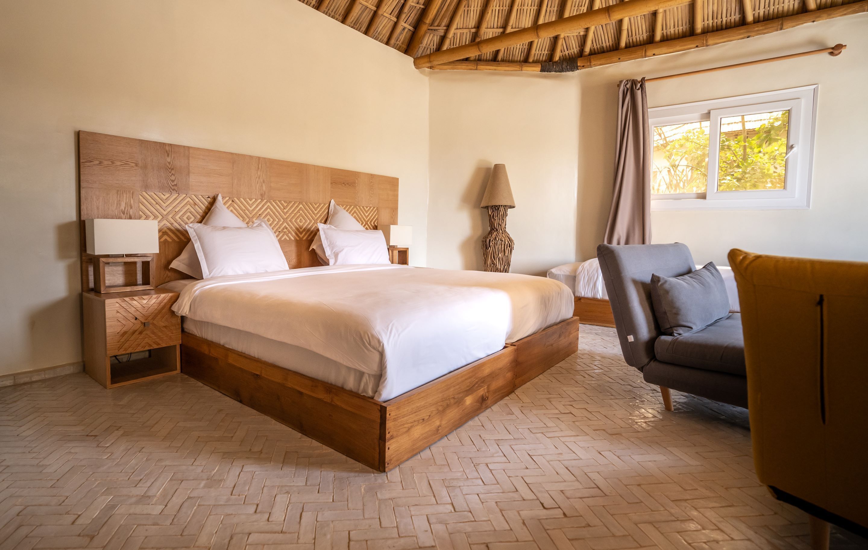 A bedroom with a wooden bed, nightstands, a lamp, a chair, and a window with a view of trees.