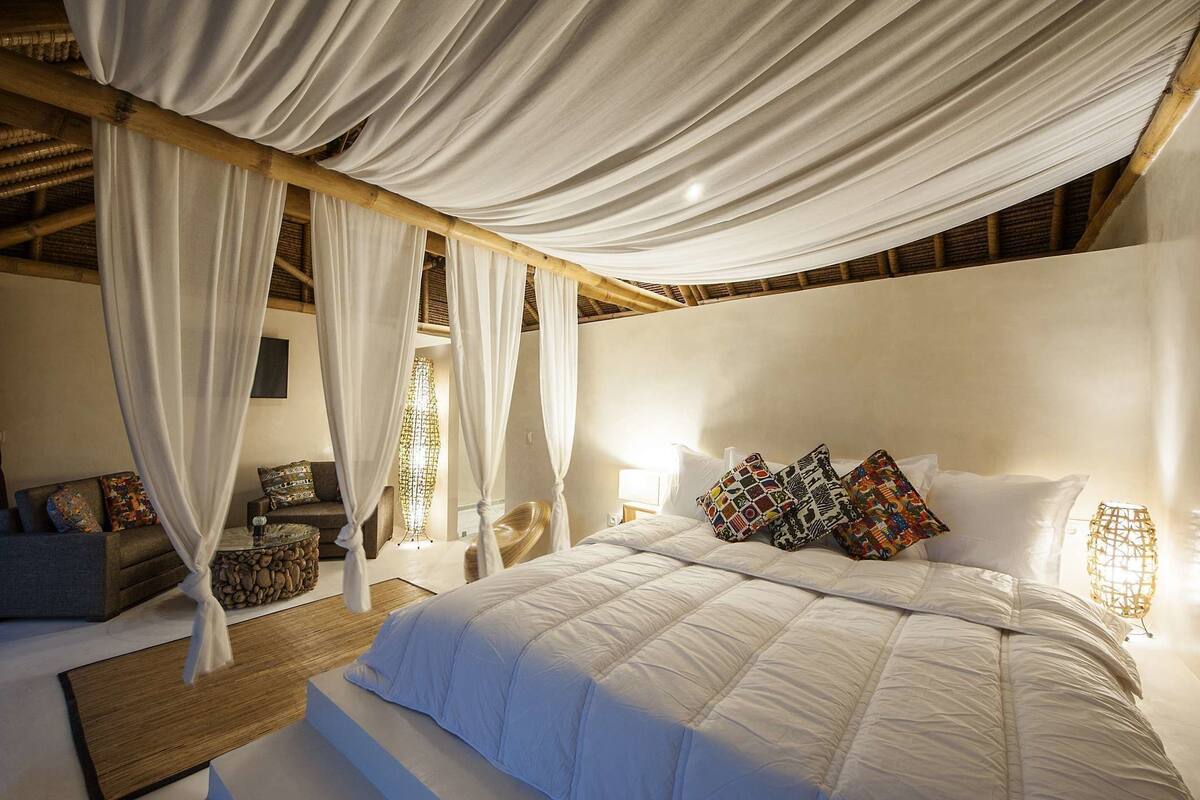 Ein Schlafzimmer mit Bett, Vorhängen, einem Sofa, einem kleinen Tisch und einer Lampe.