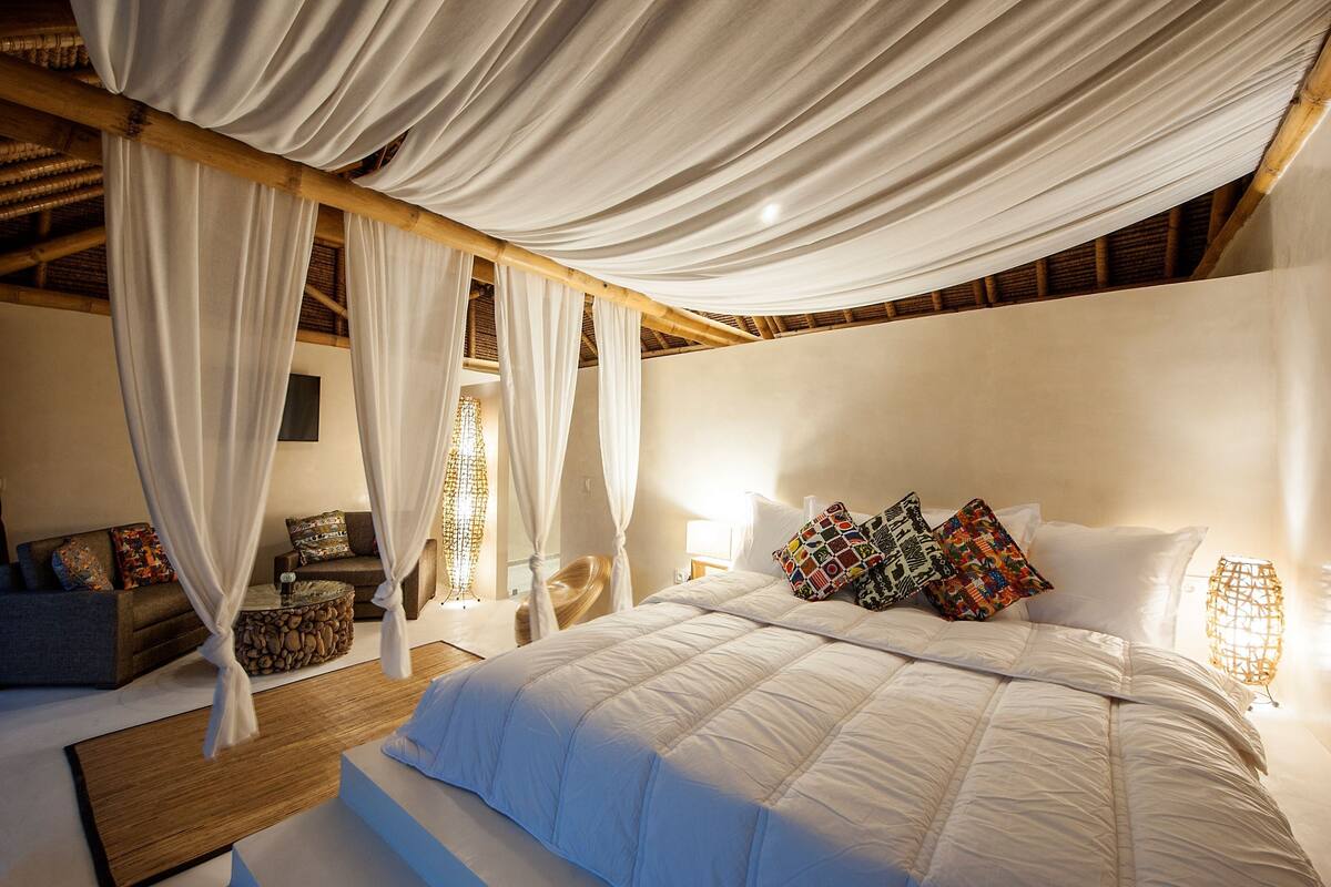 Ein Schlafzimmer mit einem großen Bett, weißen Vorhängen, einem Holzkopfende und einem Nachttisch.