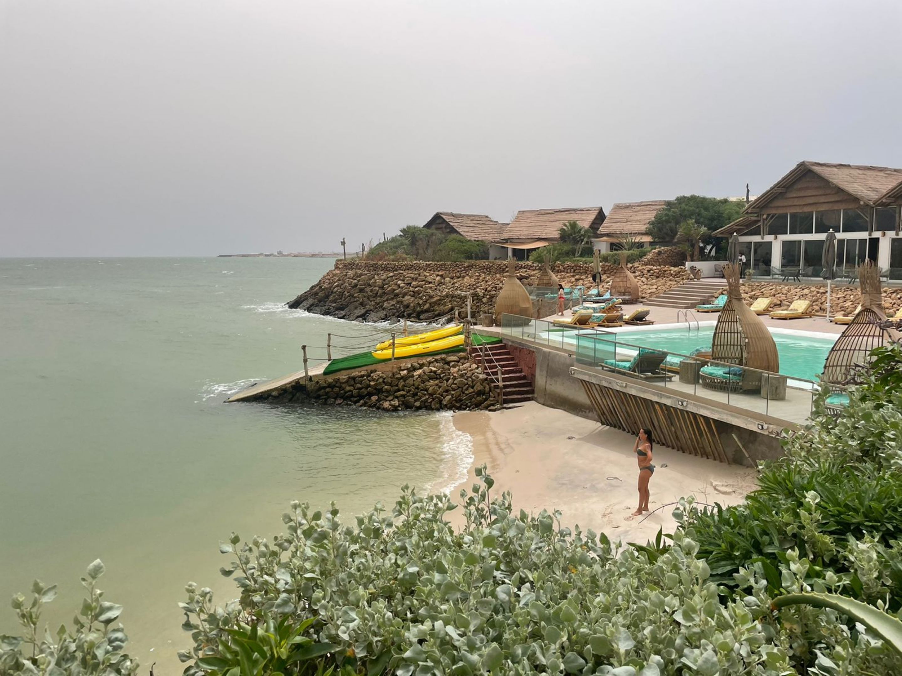 A beachside resort with a pool, lounge chairs, and a rocky breakwater.