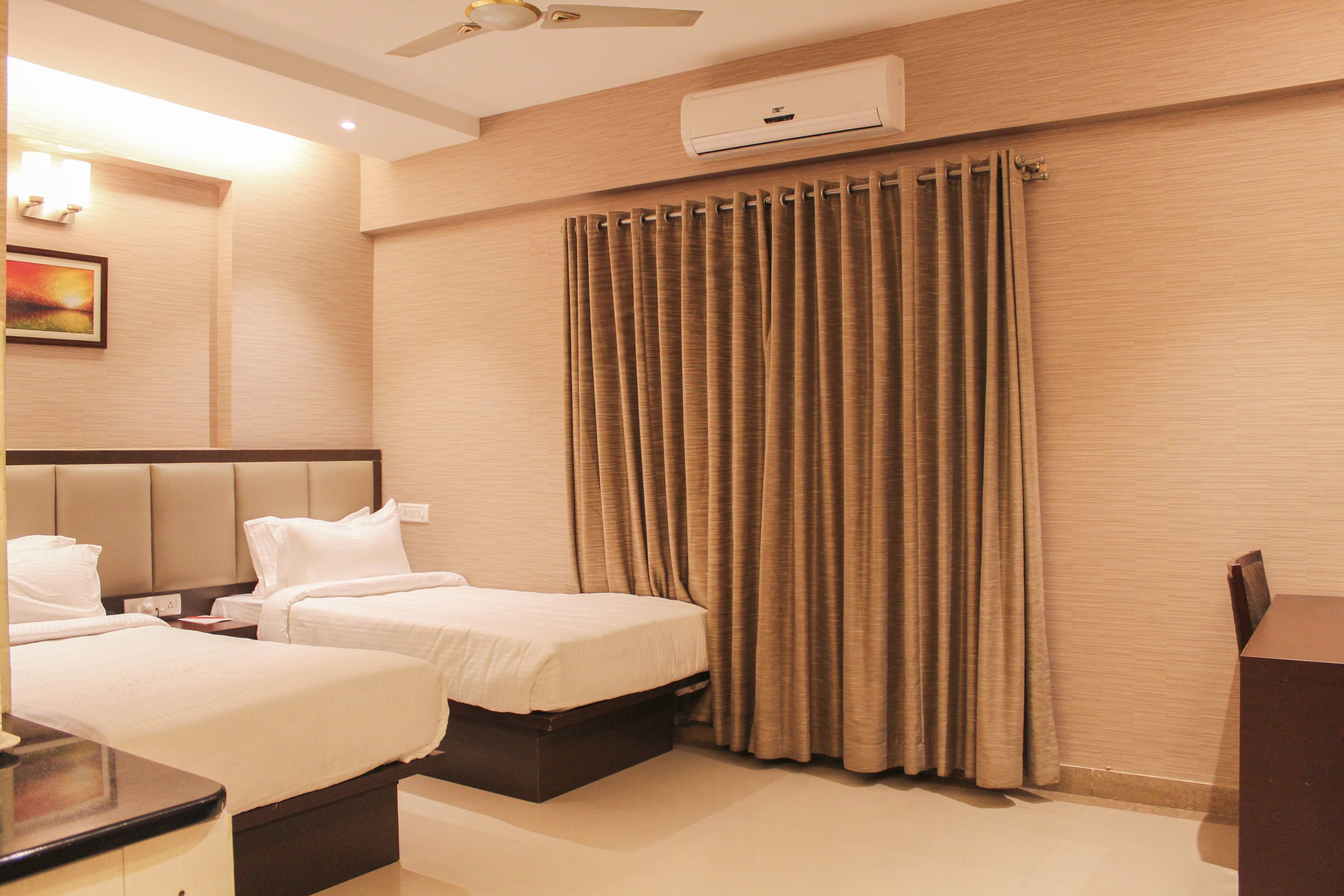 A hotel room with two beds, a ceiling fan, an air conditioning unit, and a painting on the wall.