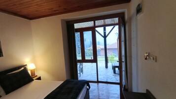 Un dormitorio con cama, mesita de noche con lámpara y puerta corrediza de vidrio que da a un patio exterior con mesa y sillas.