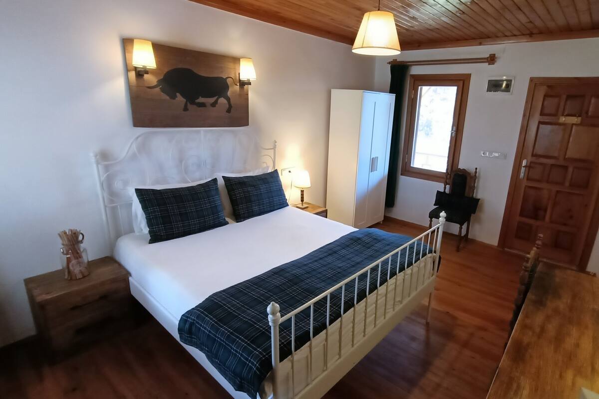 Un dormitorio con cama, mesitas de noche, armario, lámpara y un cuadro de un toro en la pared.