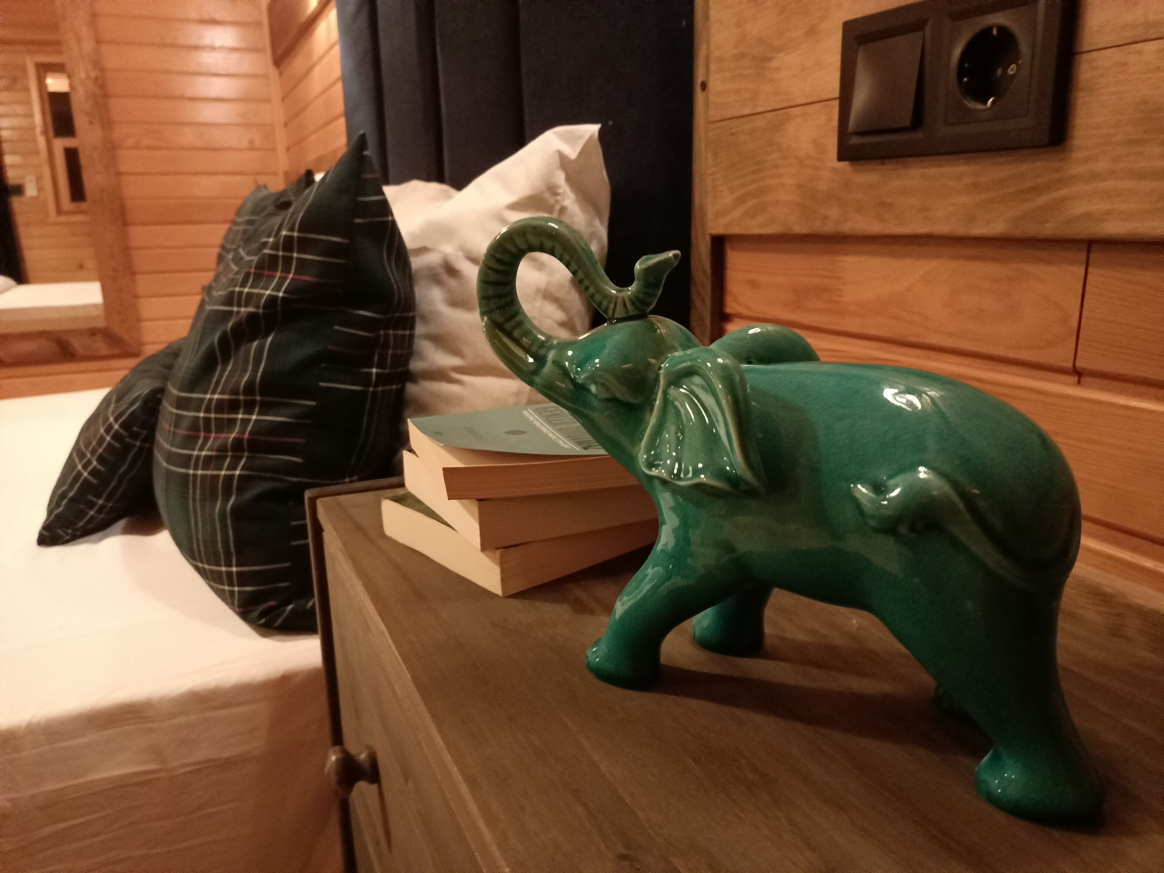 A wooden dresser with a green elephant figurine, a plaid pillow, and a stack of books.