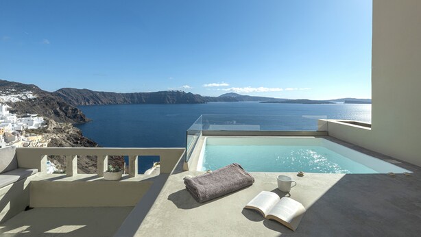 A balcony with a view of the sea, a small pool, and a book and cup on the floor. - Caldera Houses (Santorini)