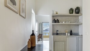 A hallway leading to a kitchen with a view, featuring a dark floor, light walls, and a door leading to a balcony. - Caldera Houses (Santorini)
