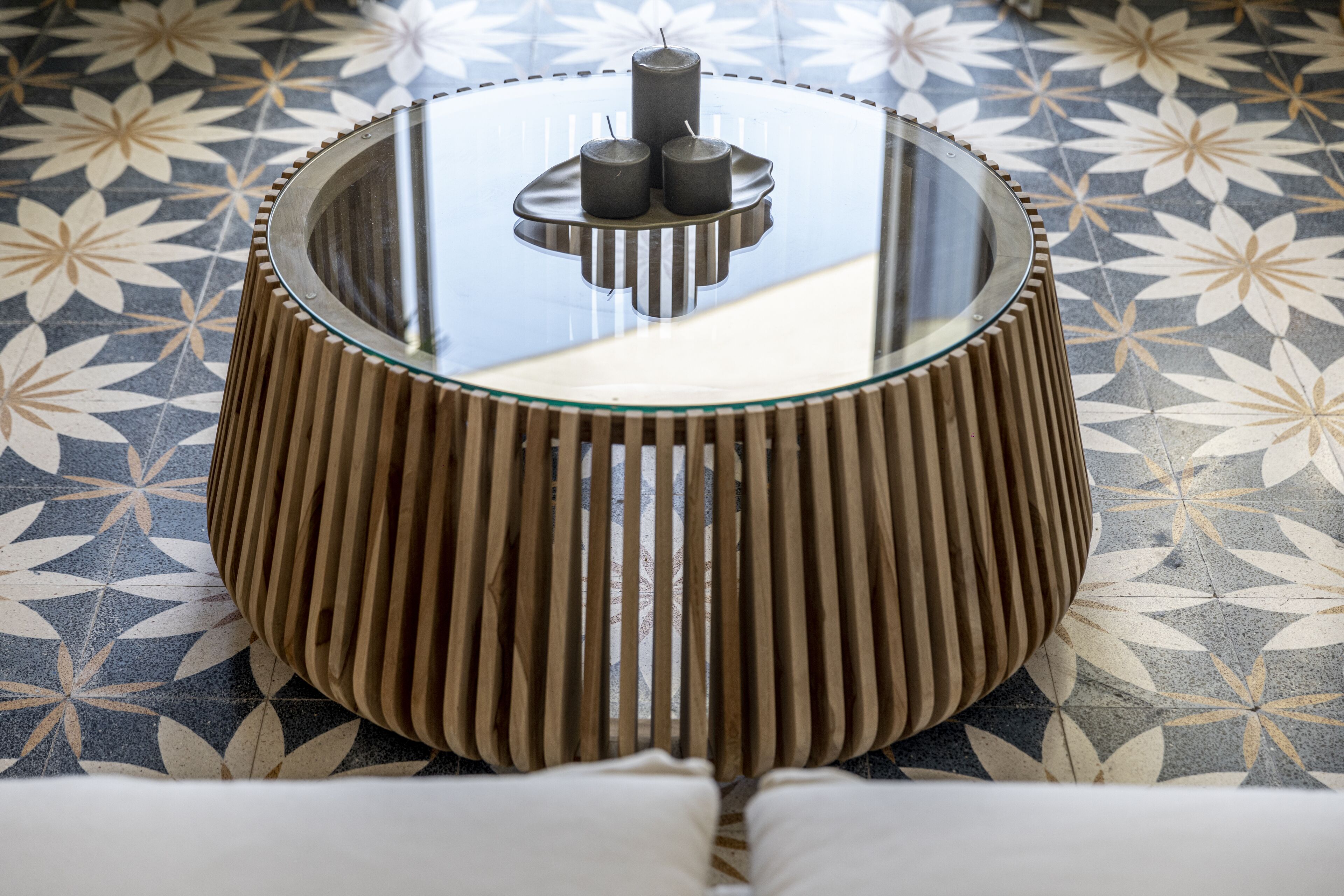 Une table ronde avec un plateau en verre et un piétement en bois composé de lattes verticales.
