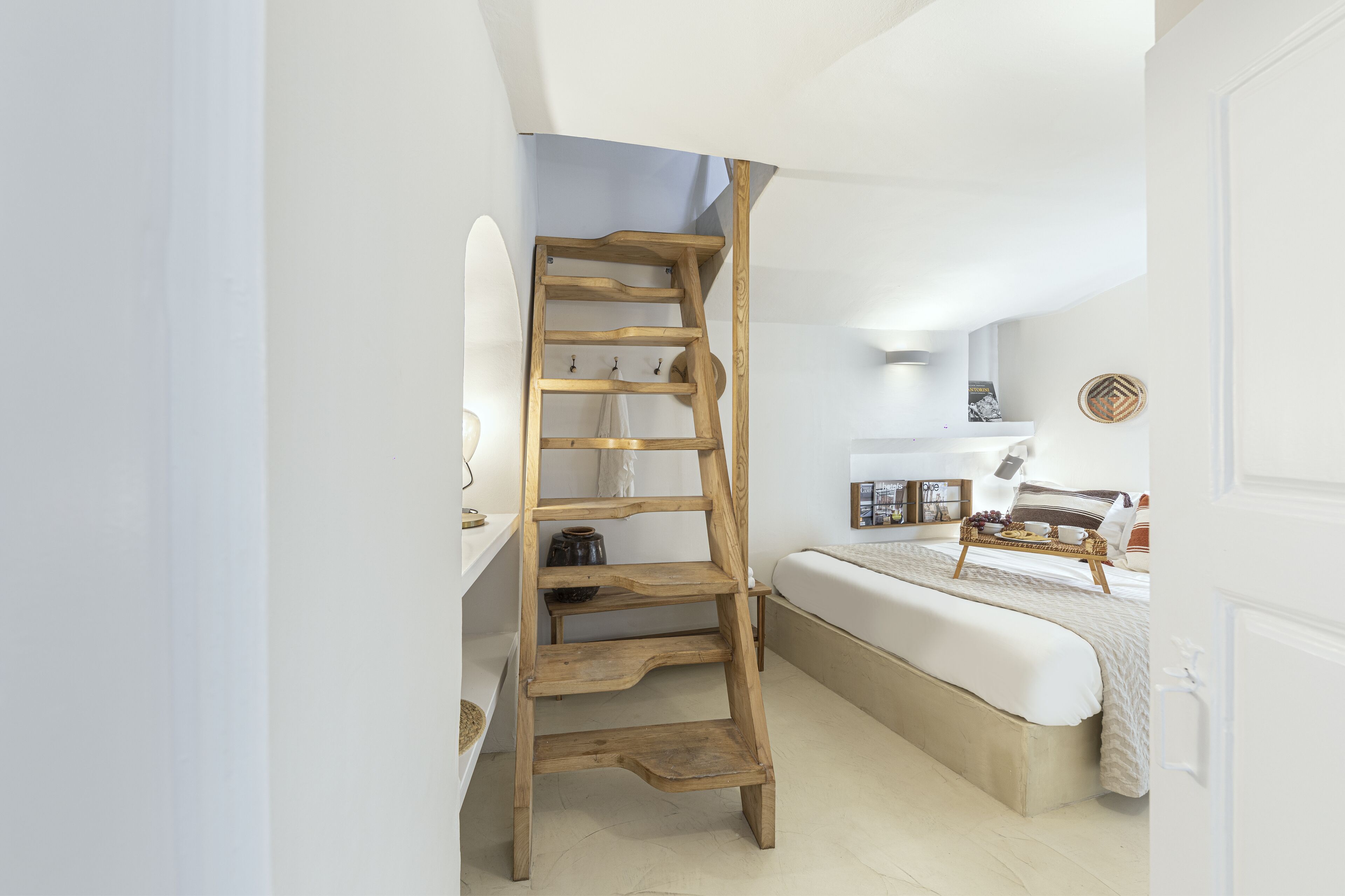 Un dormitorio con una escalera de madera, una cama, una mesita de noche y una estantería de pared.