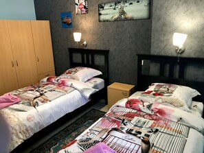 A bedroom with two beds, a wardrobe, and wall-mounted lights.