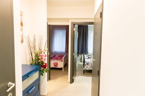 A hallway leading to a bedroom with a bed, a dresser, and a vase of flowers.