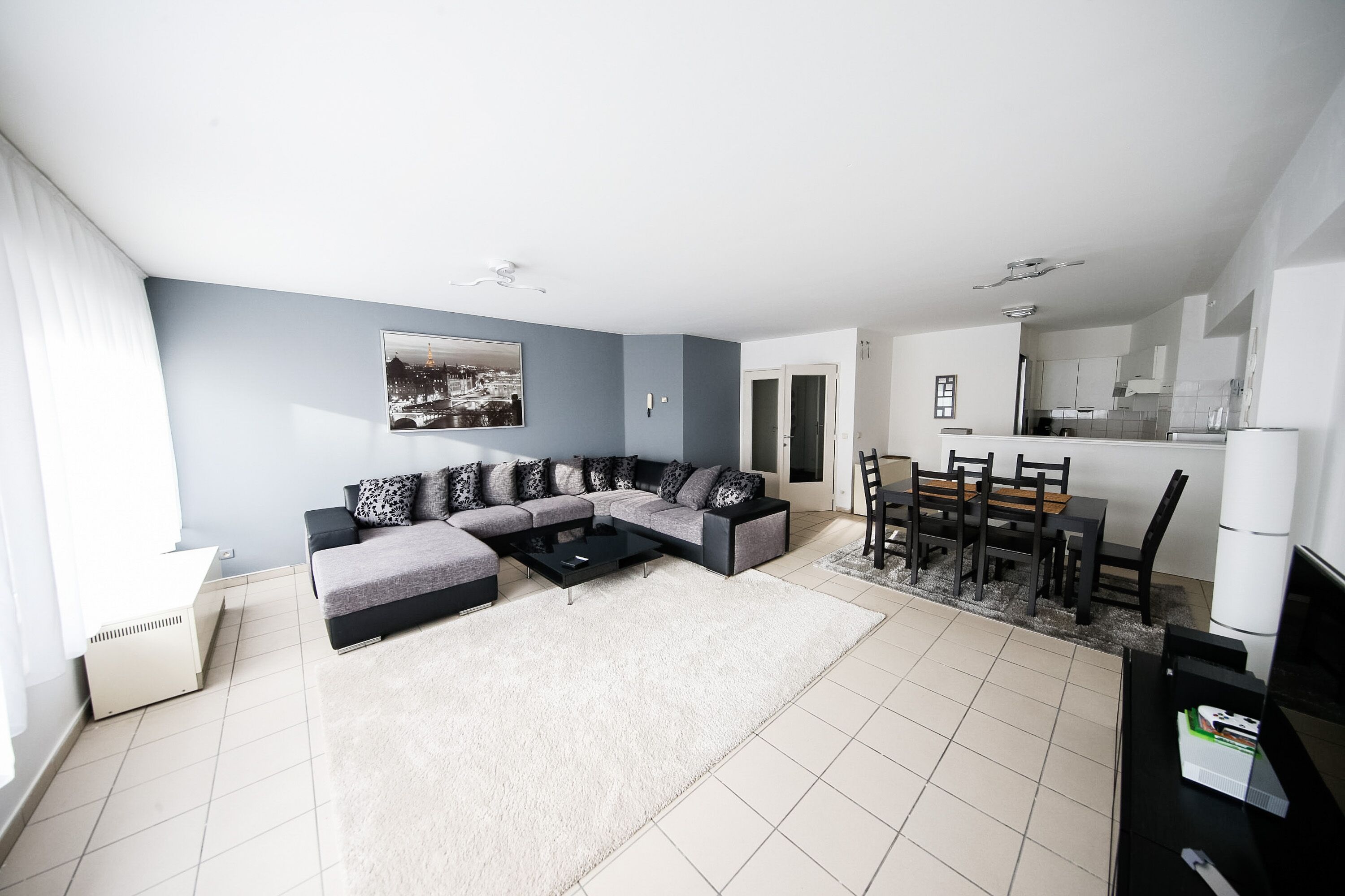 A modern living room with a sectional sofa, a dining table with chairs, and a kitchen area in the background.