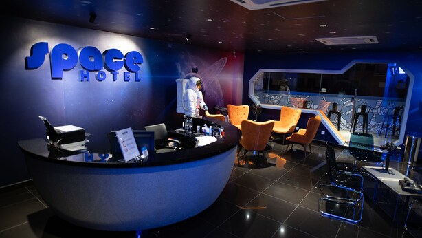 A reception area with a curved desk, several chairs, and a wall with a 'Space Hotel' sign. - Space Hotel (Kuala Lumpur)