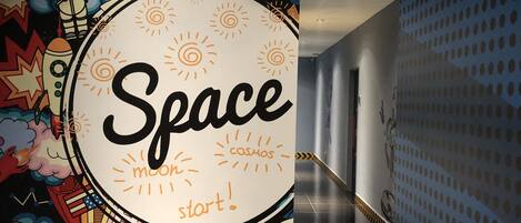 A corridor with a colorful mural featuring space-themed artwork and a sign that reads "Space moon start!"