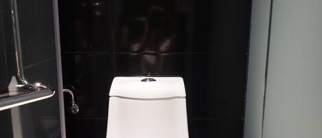 Un baño con inodoro blanco, cabina de ducha de vidrio y paredes con azulejos negros.
