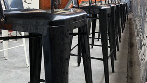 Rows of black bar stools with a ceiling featuring a geometric pattern and space-themed murals. - Space Hotel (Kuala Lumpur)