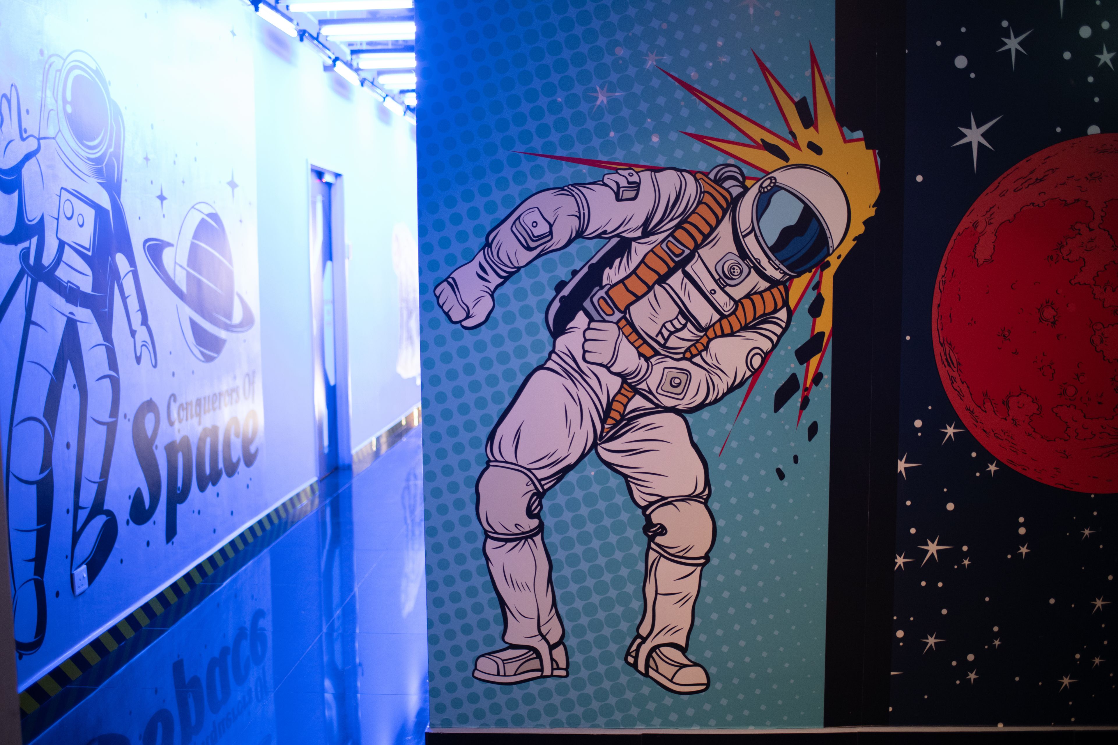 Un mur orné d’une fresque sur le thème de l’espace, représentant notamment un astronaute et une planète.