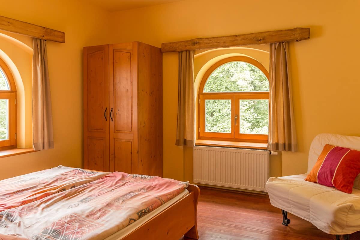 A bedroom with a bed, a wooden wardrobe, a window with an arched top, and a radiator.