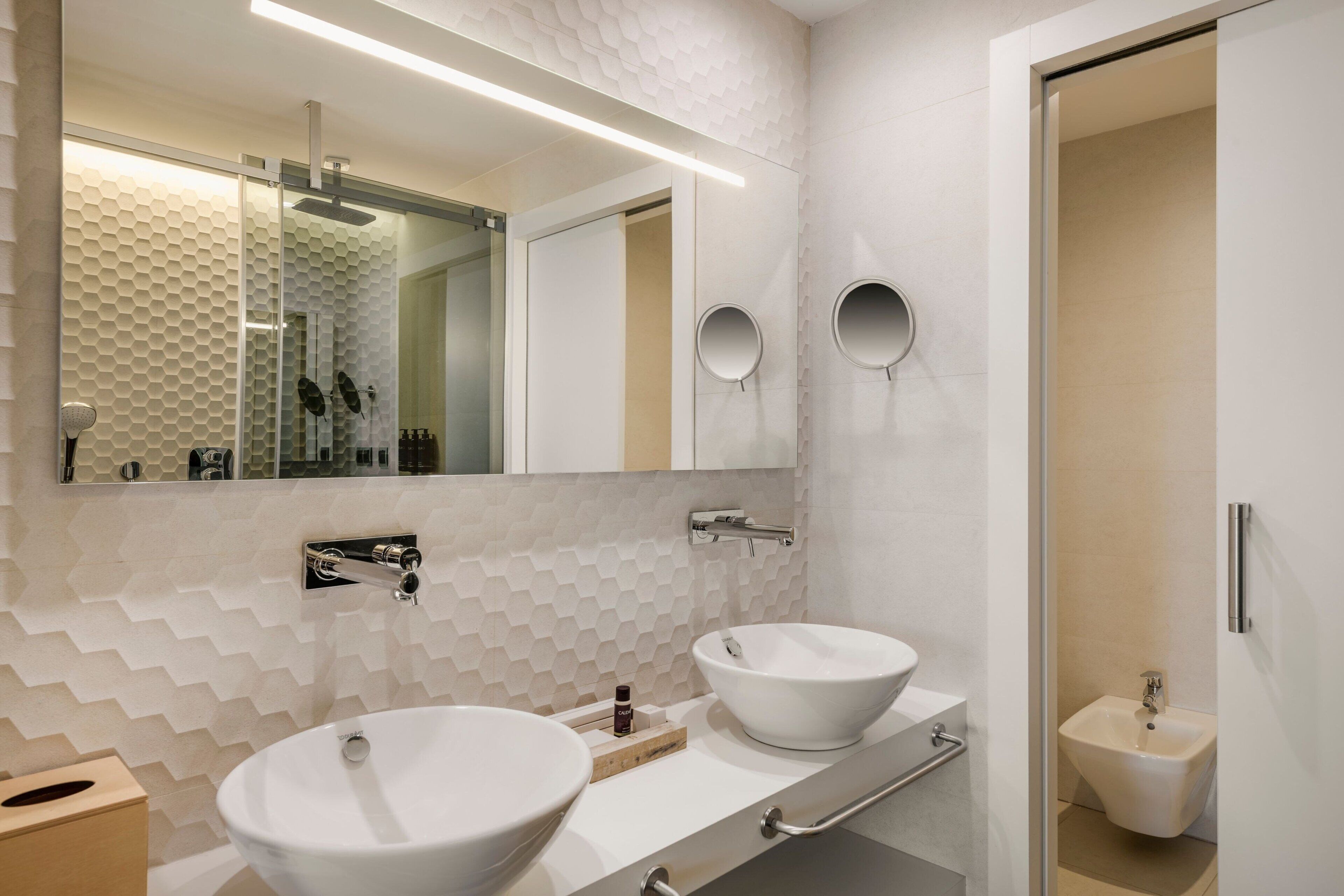 Une salle de bain moderne avec deux grands lavabos, un miroir et un bidet.