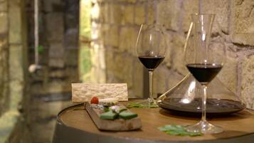 A wooden table with a wine glass, a cheese board with various cheeses and a small piece of bread, and a glass of red wine.