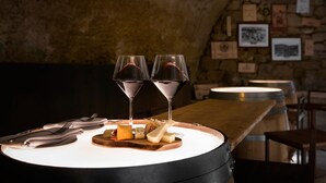 A table with a wooden board, cheese, and wine glasses in a dimly lit room with stone walls and framed pictures. - Palacio Tondon, Autograph Collection (Brinas)