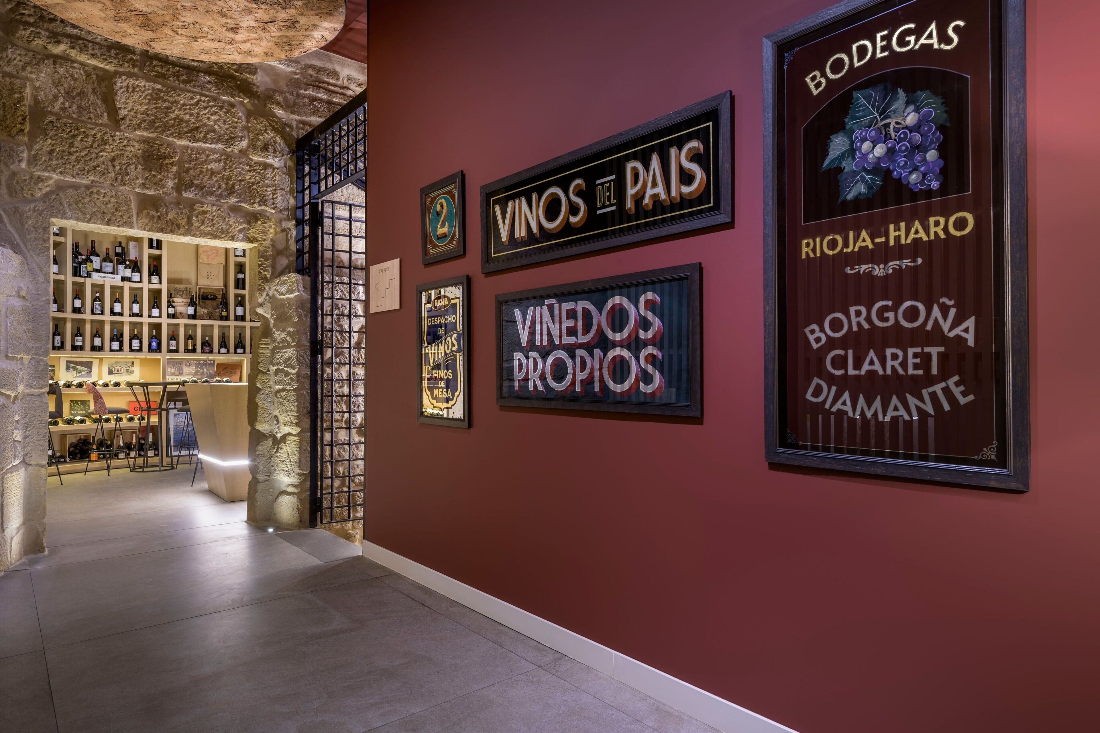 A wine cellar with shelves of bottles, a stone wall, and framed wine labels on the wall.