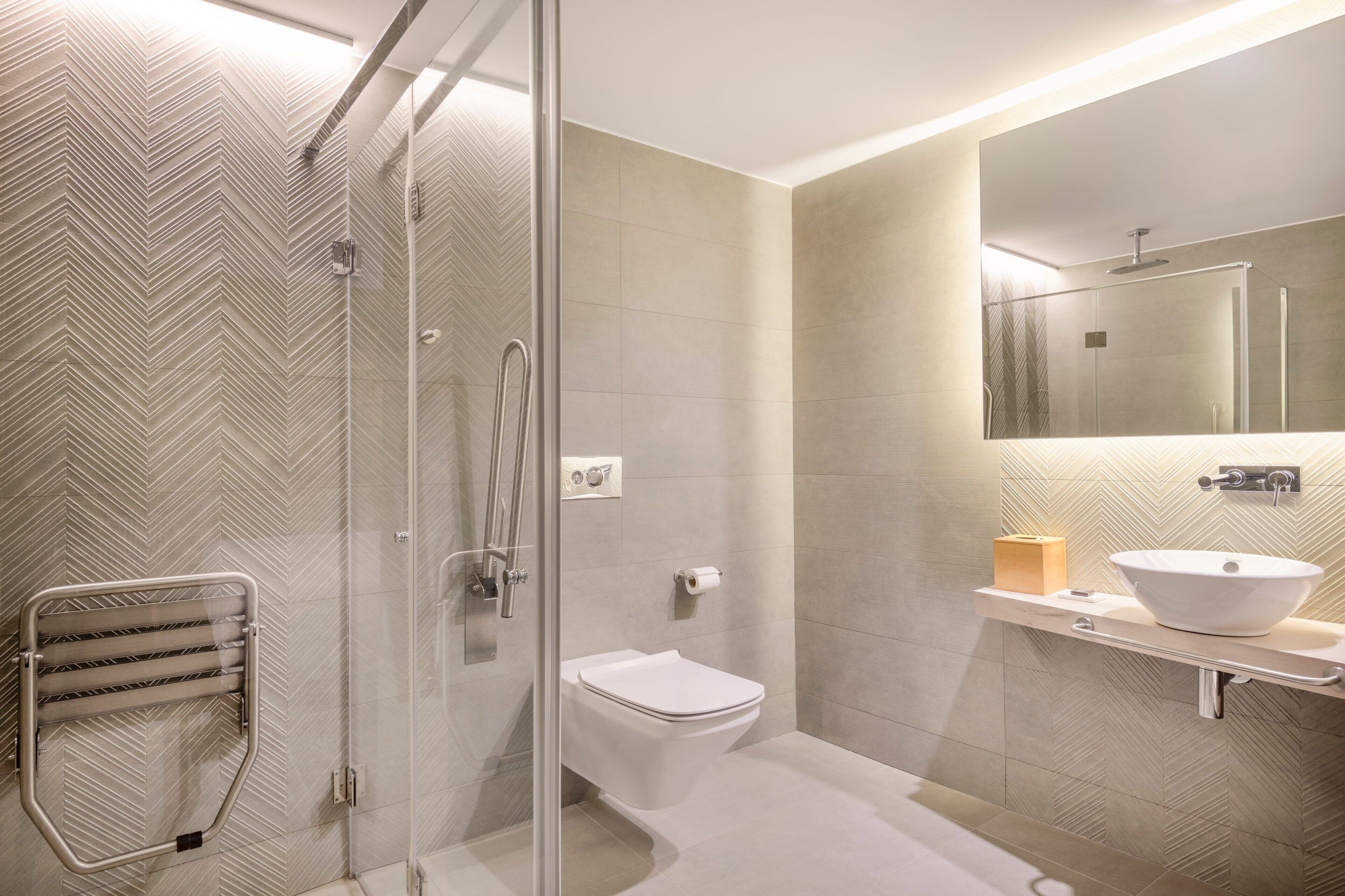 Un baño moderno con cabina de ducha de vidrio, inodoro blanco y tocador con un espejo grande y un lavabo sobre encimera.