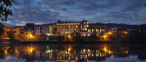 A waterfront hotel with multiple buildings, a calm lake reflecting the structures, and a clear sky.