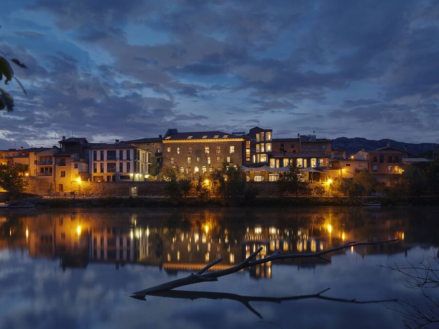 A waterfront hotel with multiple buildings, a calm lake reflecting the structures, and a clear sky.