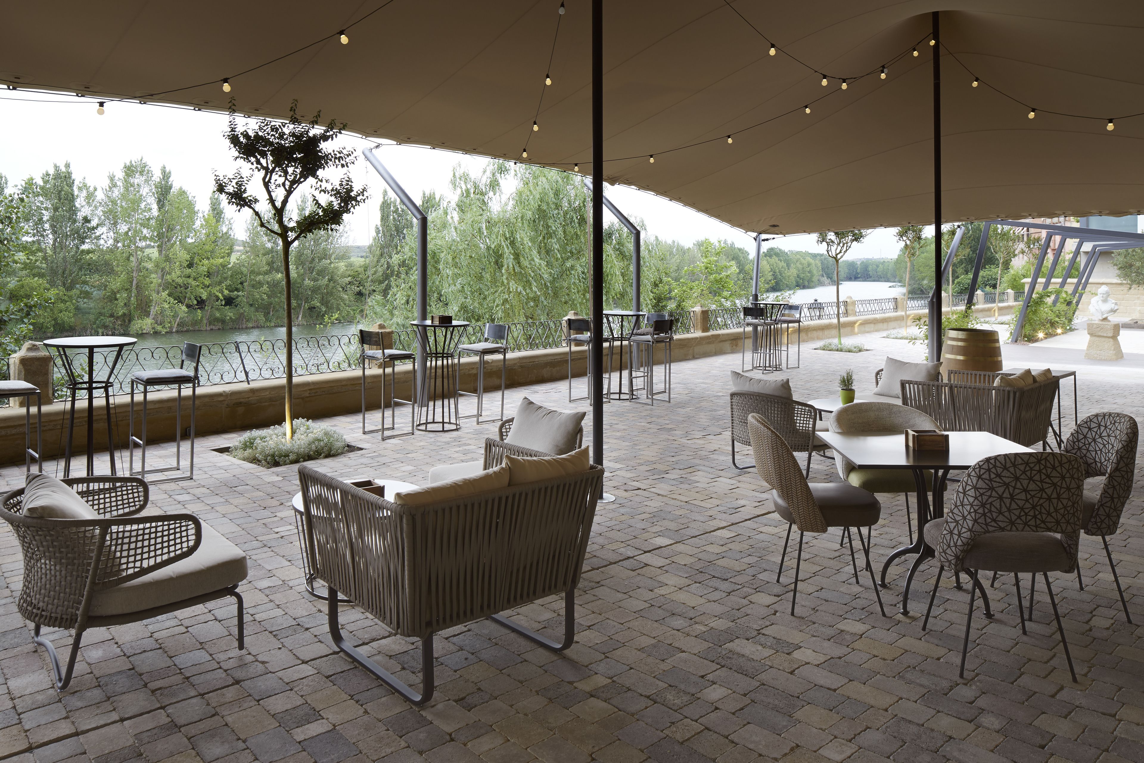 An outdoor patio with tables and chairs, a covered area, and a view of a body of water.
