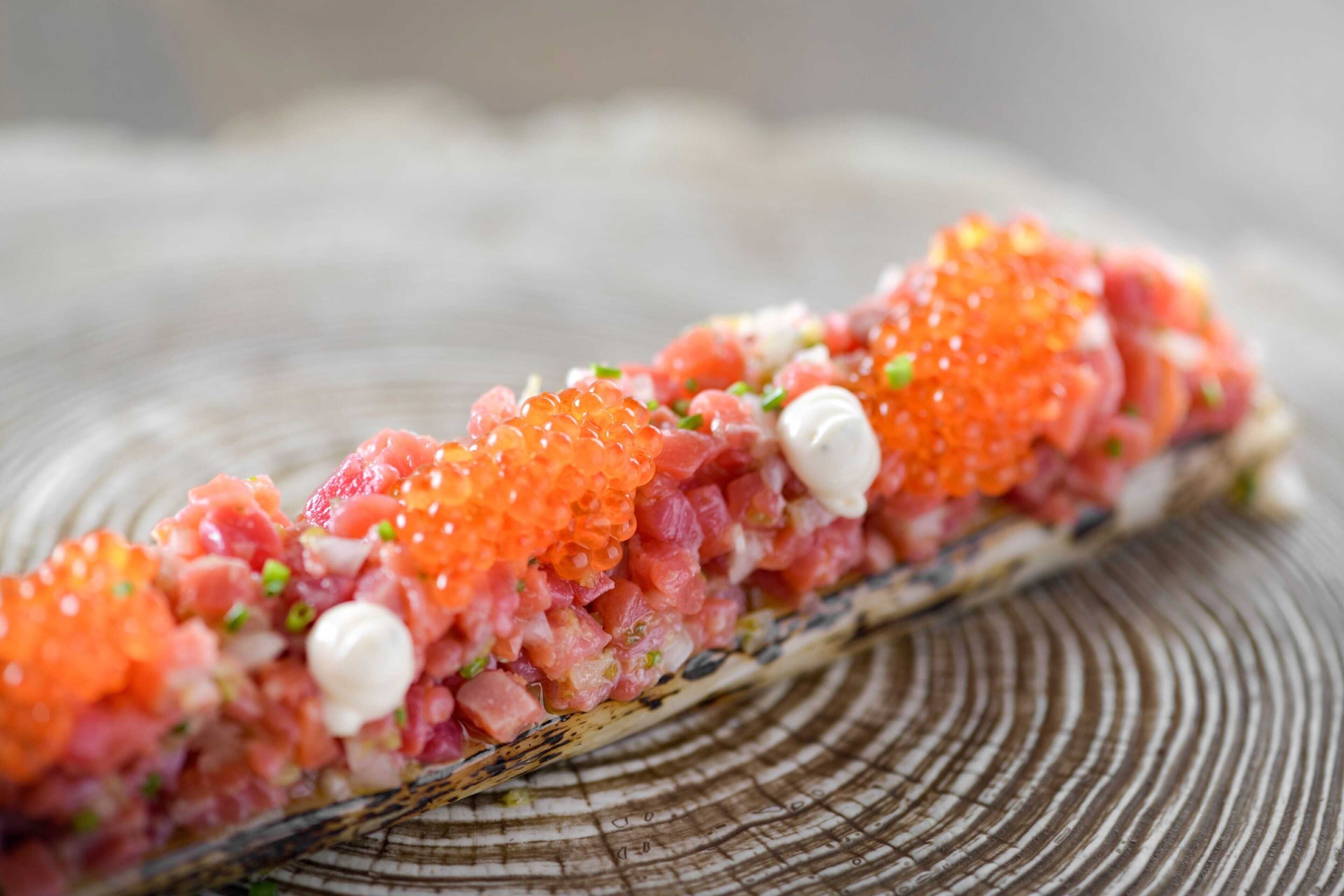 Un plato de sushi con huevas de salmón y pescado picado sobre una bandeja de madera.