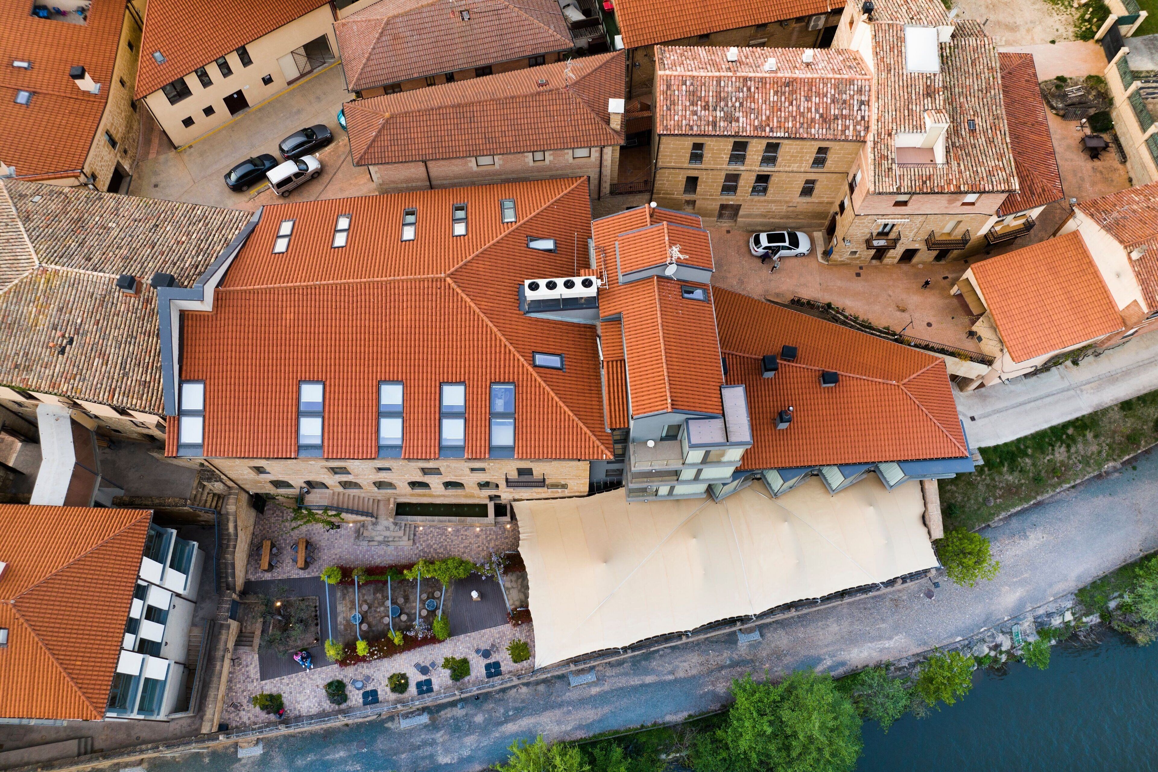 An aerial view of a historic building with a red-tiled roof, multiple windows, and a courtyard with outdoor seating.