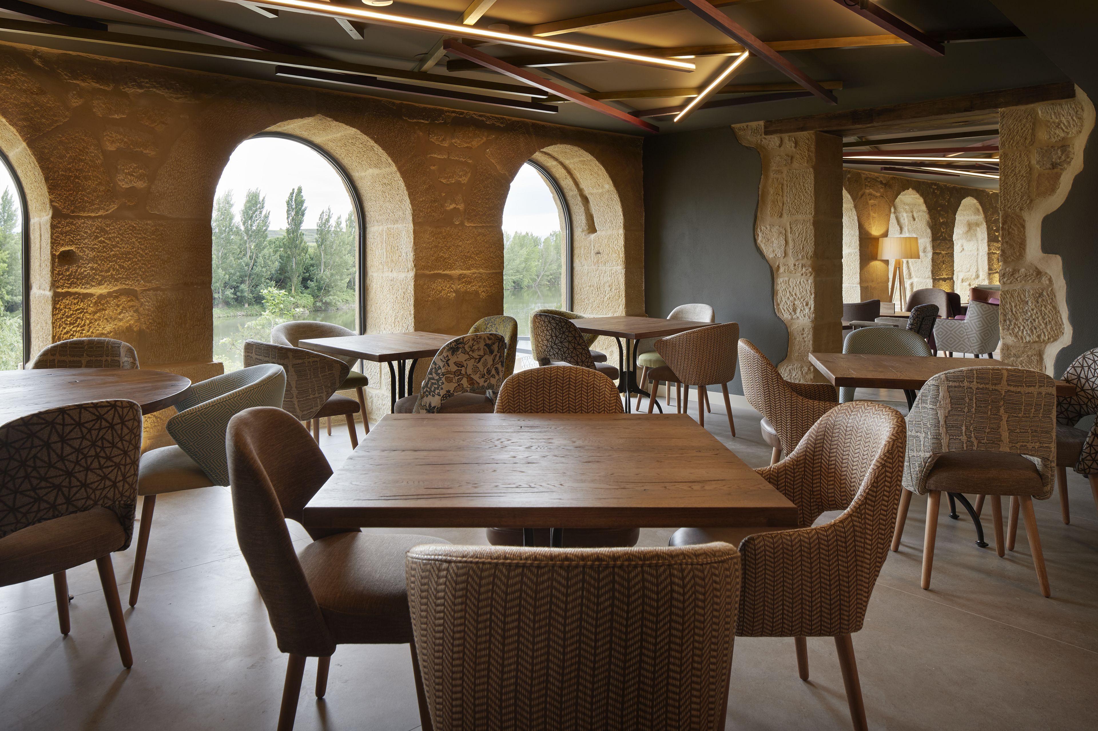 A restaurant with stone arches, wooden tables, and patterned chairs.