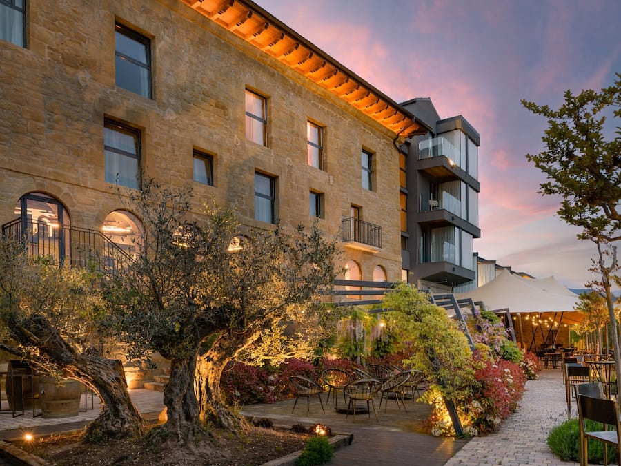 Un patio con un árbol grande, mobiliario para exteriores y un edificio con varias ventanas y balcones.